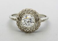 white metal ring with a large round central white stone, and stones wrapping the band